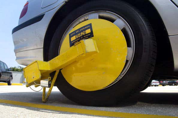 一辆停着的银色轿车的右后轮上有一个黄色的、后备箱式的拖车轮锁，侧面写着“芝加哥市”。
