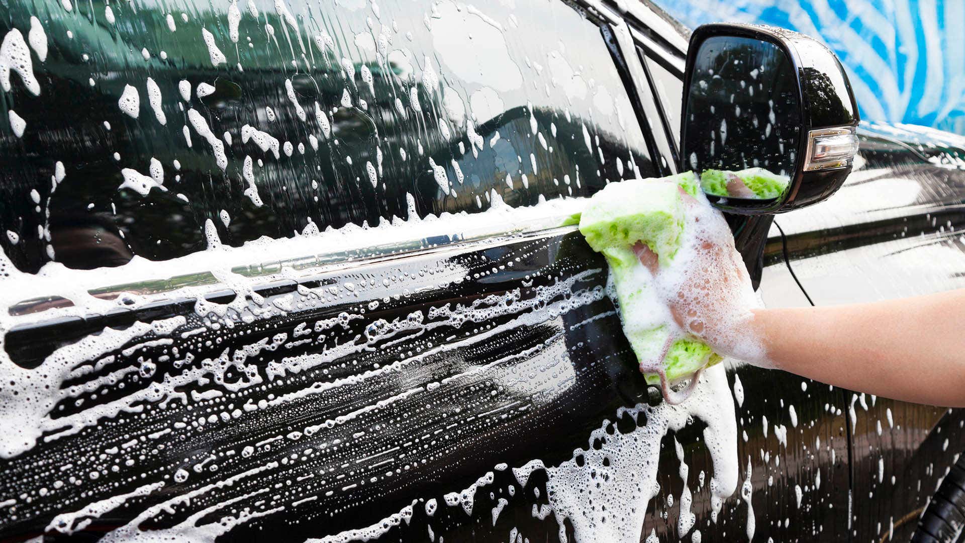 一只手正在用海绵擦拭沾有肥皂的车门。
