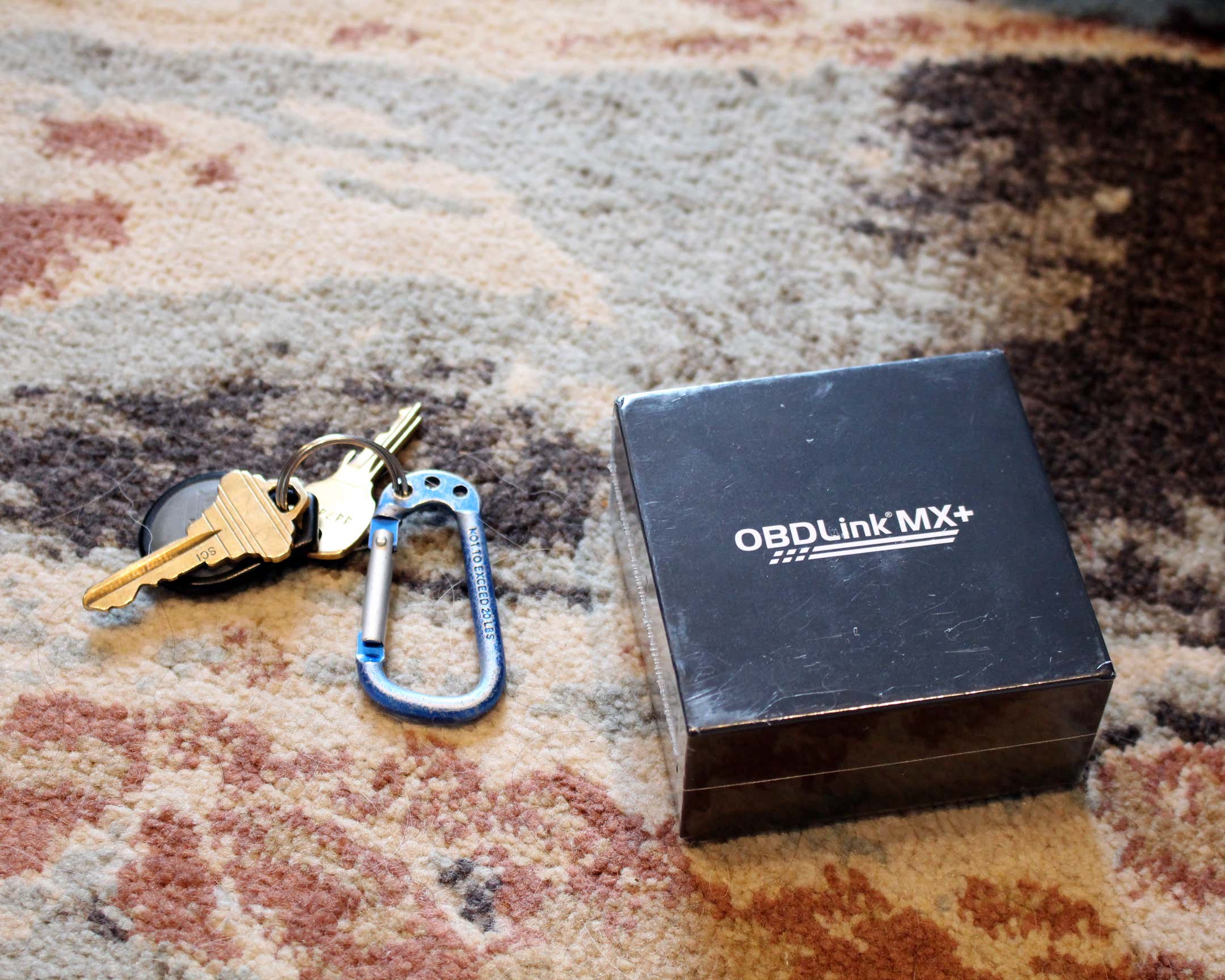 多色地毯顶部钥匙旁边的OBDLink MX+黑匣子。